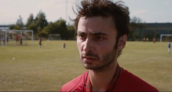Movie still from “Two Days, One Night” (2014), directed by Jean-Pierre Dardenne – A person wearing a red shirt on a soccer field; Close Up shot, Over the shoulder angle