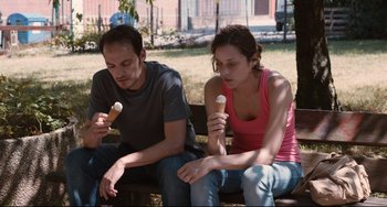Movie still from “Two Days, One Night” (2014), directed by Jean-Pierre Dardenne – A man and a woman sitting on a park bench eating ice cream; Medium shot, High angle