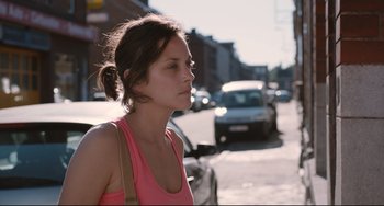 Movie still from “Two Days, One Night” (2014), directed by Jean-Pierre Dardenne – A woman in a pink shirt is standing on the side of the street; Close Up shot, Over the shoulder angle