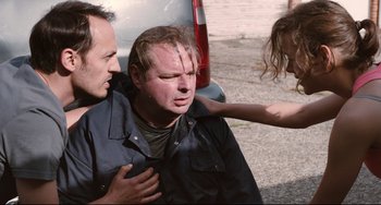 Movie still from “Two Days, One Night” (2014), directed by Jean-Pierre Dardenne – A man is being helped by two other men; Medium shot, Over the shoulder angle