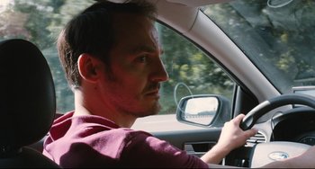 Movie still from “Two Days, One Night” (2014), directed by Jean-Pierre Dardenne – A man sitting in the drivers seat of a car; Close Up shot, Low angle