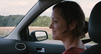 Movie still from “Two Days, One Night” (2014), directed by Jean-Pierre Dardenne – A woman sitting in the driver's seat of a car looking out the window; Close Up shot, Over the shoulder angle