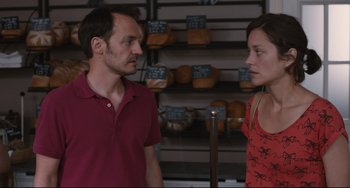 Movie still from “Two Days, One Night” (2014), directed by Jean-Pierre Dardenne – A man and a woman standing next to each other in front of shelves; Medium shot, Over the shoulder angle