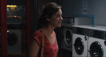Movie still from “Two Days, One Night” (2014), directed by Jean-Pierre Dardenne – A young woman standing in front of a washing machine; Medium shot, Over the shoulder angle