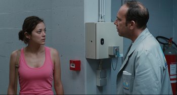 Movie still from “Two Days, One Night” (2014), directed by Jean-Pierre Dardenne – A man and a woman standing next to each other in a room; Medium shot, Over the shoulder angle