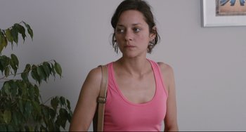 Movie still from “Two Days, One Night” (2014), directed by Jean-Pierre Dardenne – A woman in a pink tank top holding a brown bag; Close Up shot, High angle