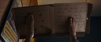 Movie still from “Under the Silver Lake” (2018), directed by David Robert Mitchell – A person holding open a box that has writing on it; Extreme Close Up shot, High angle