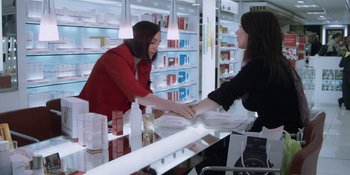 Movie still from “Under the Skin” (2013), directed by Jonathan Glazer – A woman is shaking hands with another woman in a store; Medium shot, Over the shoulder angle