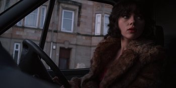 Movie still from “Under the Skin” (2013), directed by Jonathan Glazer – A woman sitting in the drivers seat of a car; Medium shot, Over the shoulder angle