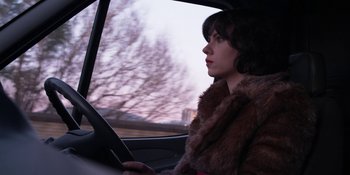 Movie still from “Under the Skin” (2013), directed by Jonathan Glazer – A woman sitting in the drivers seat of a car looking out the window; Medium shot, Over the shoulder angle