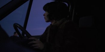 Movie still from “Under the Skin” (2013), directed by Jonathan Glazer – A woman sitting in a car looking out the window at night; Medium shot, Over the shoulder angle