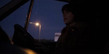 Movie still from “Under the Skin” (2013), directed by Jonathan Glazer – A woman sitting in the driver's seat of a car at night; Medium shot, Over the shoulder angle