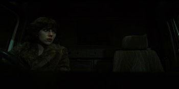 Movie still from “Under the Skin” (2013), directed by Jonathan Glazer – A woman wearing a fur coat sitting in a dark room; Medium shot, Low angle