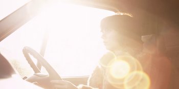 Movie still from “Under the Skin” (2013), directed by Jonathan Glazer – A woman sitting in the driver's seat of a car; Medium shot, Low angle