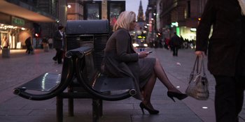 Movie still from “Under the Skin” (2013), directed by Jonathan Glazer – A woman sitting on top of a bench on the sidewalk; Wide shot, Low angle