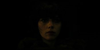 Movie still from “Under the Skin” (2013), directed by Jonathan Glazer – A woman with dark hair is looking at the camera; Close Up shot, Overhead angle