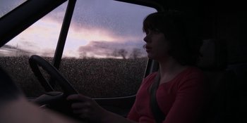 Movie still from “Under the Skin” (2013), directed by Jonathan Glazer – A woman sitting in the driver's seat of a car looking out the window; Medium shot, Low angle