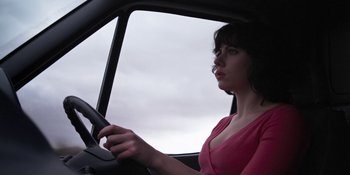 Movie still from “Under the Skin” (2013), directed by Jonathan Glazer – A woman sitting in the driver's seat of a car; Medium shot, Low angle