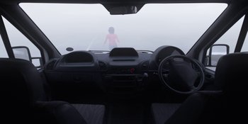 Movie still from “Under the Skin” (2013), directed by Jonathan Glazer – A person standing in a car on a foggy day; Wide shot, High angle
