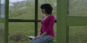 Movie still from “Under the Skin” (2013), directed by Jonathan Glazer – A woman sitting on top of a bench near a window; Medium shot, High angle