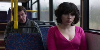 Movie still from “Under the Skin” (2013), directed by Jonathan Glazer – A woman sitting on a public bus with a man standing behind her; Medium shot, Over the shoulder angle