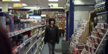 Movie still from “Under the Skin” (2013), directed by Jonathan Glazer – A woman is walking through a store filled with lots of cards; Medium shot, Low angle