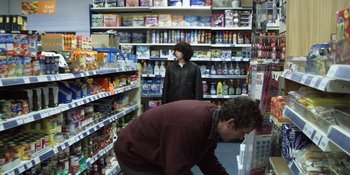 Movie still from “Under the Skin” (2013), directed by Jonathan Glazer – A man and a woman in a grocery store; Wide shot, Over the shoulder angle