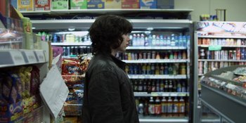 Movie still from “Under the Skin” (2013), directed by Jonathan Glazer – A person standing in front of a shelf in a grocery store; Medium shot, Over the shoulder angle