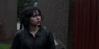 Movie still from “Under the Skin” (2013), directed by Jonathan Glazer – A woman in black jacket standing next to a wall; Close Up shot, Over the shoulder angle