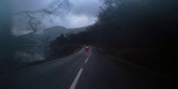 Movie still from “Under the Skin” (2013), directed by Jonathan Glazer – A car driving down a road in the dark; Extreme Wide shot, High angle