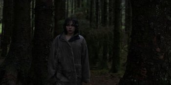 Movie still from “Under the Skin” (2013), directed by Jonathan Glazer – A person standing in the middle of a forest; Wide shot, Over the shoulder angle