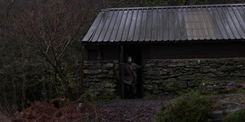 Movie still from “Under the Skin” (2013), directed by Jonathan Glazer – A man standing in front of a stone building; Wide shot, Low angle