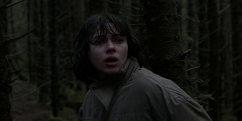 Movie still from “Under the Skin” (2013), directed by Jonathan Glazer – A person standing next to a tree in the woods; Medium shot, Low angle