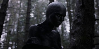 Movie still from “Under the Skin” (2013), directed by Jonathan Glazer – A statue of a person in the woods; Close Up shot, Low angle