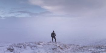 Movie still from “Under the Skin” (2013), directed by Jonathan Glazer – A man standing on a surfboard in the ocean; Extreme Wide shot, Low angle
