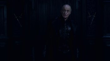 Movie still from “Underworld: Blood Wars” (2016), directed by Anna Foerster – An older man in a black jacket standing in front of a wooden wall; Medium shot, Low angle