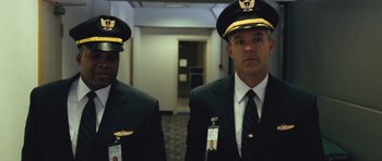 Movie still from “United 93” (2006), directed by Paul Greengrass – Two men in suits and hats standing next to each other in a hallway; Medium shot, Low angle