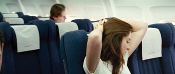 Movie still from “United 93” (2006), directed by Paul Greengrass – A woman sitting on an airplane holding her head in her hands; Medium shot, Over the shoulder angle