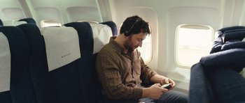 Movie still from “United 93” (2006), directed by Paul Greengrass – A man sitting on an airplane looking at his phone; Medium shot, High angle