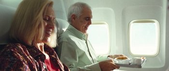 Movie still from “United 93” (2006), directed by Paul Greengrass – An older man sitting on a plane while a woman looks at him; Medium shot, High angle