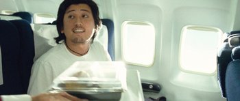 Movie still from “United 93” (2006), directed by Paul Greengrass – A man sitting on top of an airplane holding a tray; Medium shot, Overhead angle