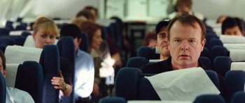 Movie still from “United 93” (2006), directed by Paul Greengrass – A group of people sitting on a blue airplane seat; Medium shot, Over the shoulder angle