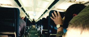Movie still from “United 93” (2006), directed by Paul Greengrass – A person with a watch is sitting on a seat on an airplane; Medium shot, Overhead angle
