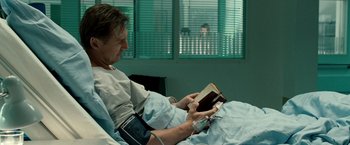 Movie still from “Unknown” (2011), directed by Jaume Collet-Serra – A man in a hospital bed reading a book; Medium shot, Over the shoulder angle