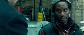 Movie still from “Unknown” (2011), directed by Jaume Collet-Serra – A man wearing a jacket and hat in a warehouse; Close Up shot, Over the shoulder angle