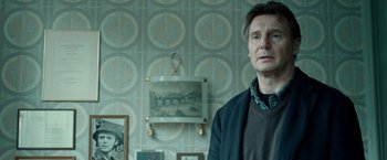 Movie still from “Unknown” (2011), directed by Jaume Collet-Serra – Liam neeson stands in front of a wall with pictures on it; Medium shot, Low angle