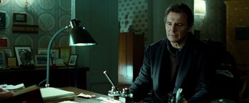 Movie still from “Unknown” (2011), directed by Jaume Collet-Serra – A man sitting at a table in front of a lamp; Medium shot, Low angle