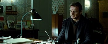 Movie still from “Unknown” (2011), directed by Jaume Collet-Serra – A man sitting at a desk in a room; Medium shot, Low angle
