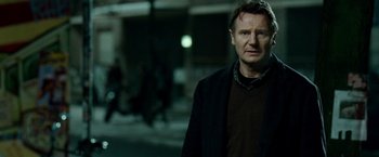 Movie still from “Unknown” (2011), directed by Jaume Collet-Serra – A man standing on the sidewalk in the dark; Medium shot, Over the shoulder angle