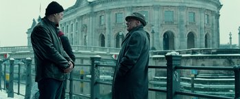 Movie still from “Unknown” (2011), directed by Jaume Collet-Serra – A man wearing a coat and hat standing next to a railing; Medium shot, Over the shoulder angle